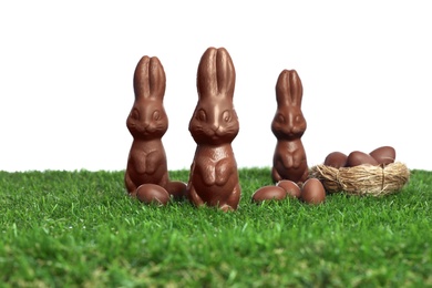 Chocolate bunnies and eggs on green grass against white background. Easter celebration