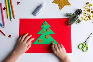 Photo of Little child making Christmas card at white table, top view