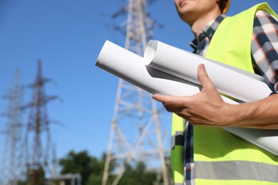 Photo of Professional electrician with draftings near high voltage tower, closeup