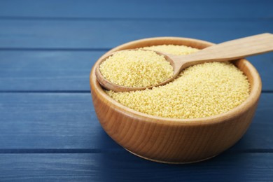 Bowl and spoon with raw couscous on blue wooden table, closeup. Space for text