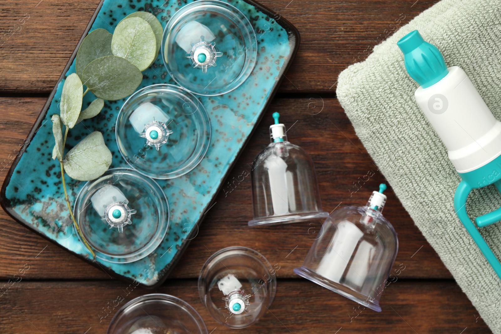 Photo of Cupping therapy. Plastic cups, hand pump, towel and eucalyptus leaves on wooden table, flat lay