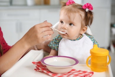 Photo of Mother feeding her little baby with healthy food in kitchen