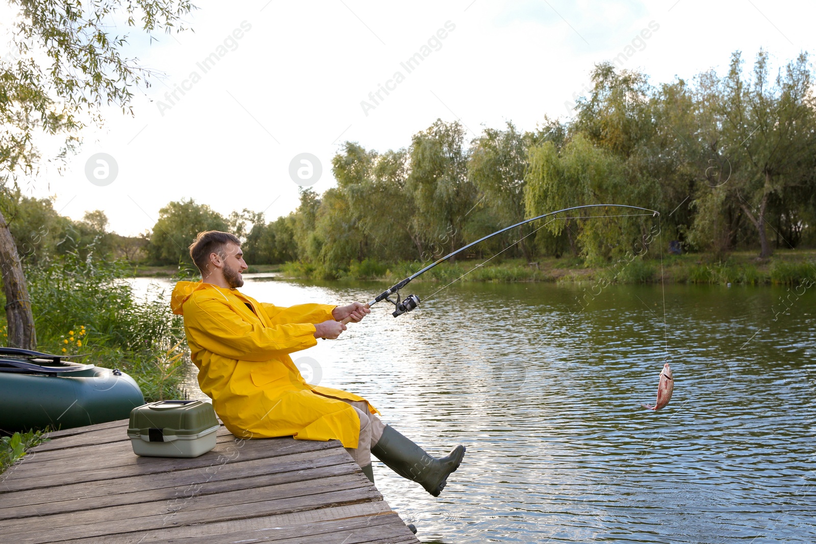 Photo of Man with rod fishing on wooden pier at riverside. Recreational activity