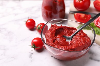 Photo of Glass bowl of tasty tomato paste with spoon and ingredients on white marble table, closeup. Space for text