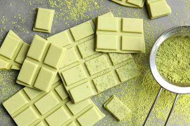 Pieces of tasty matcha chocolate bars and powder on grey table, flat lay