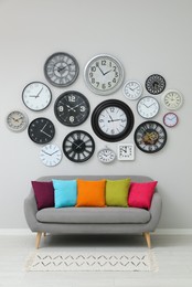 Sofa and many different clocks hanging on white wall in room