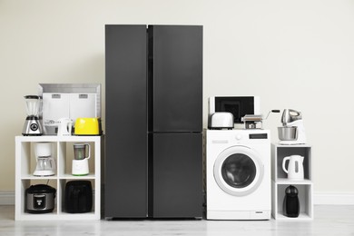 Photo of Modern refrigerator and other household appliances near beige wall indoors