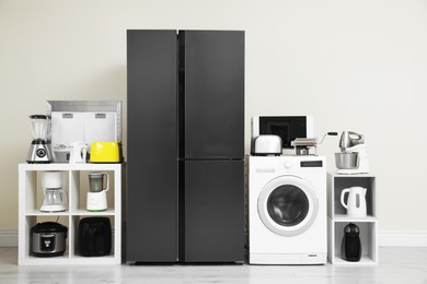 Modern refrigerator and other household appliances near beige wall indoors