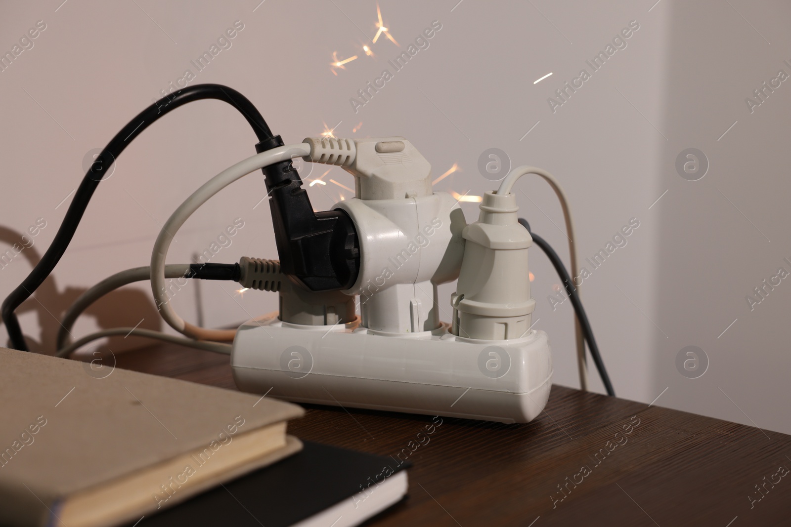 Photo of Inflamed plug in power strip indoors on wooden table. Electrical short circuit