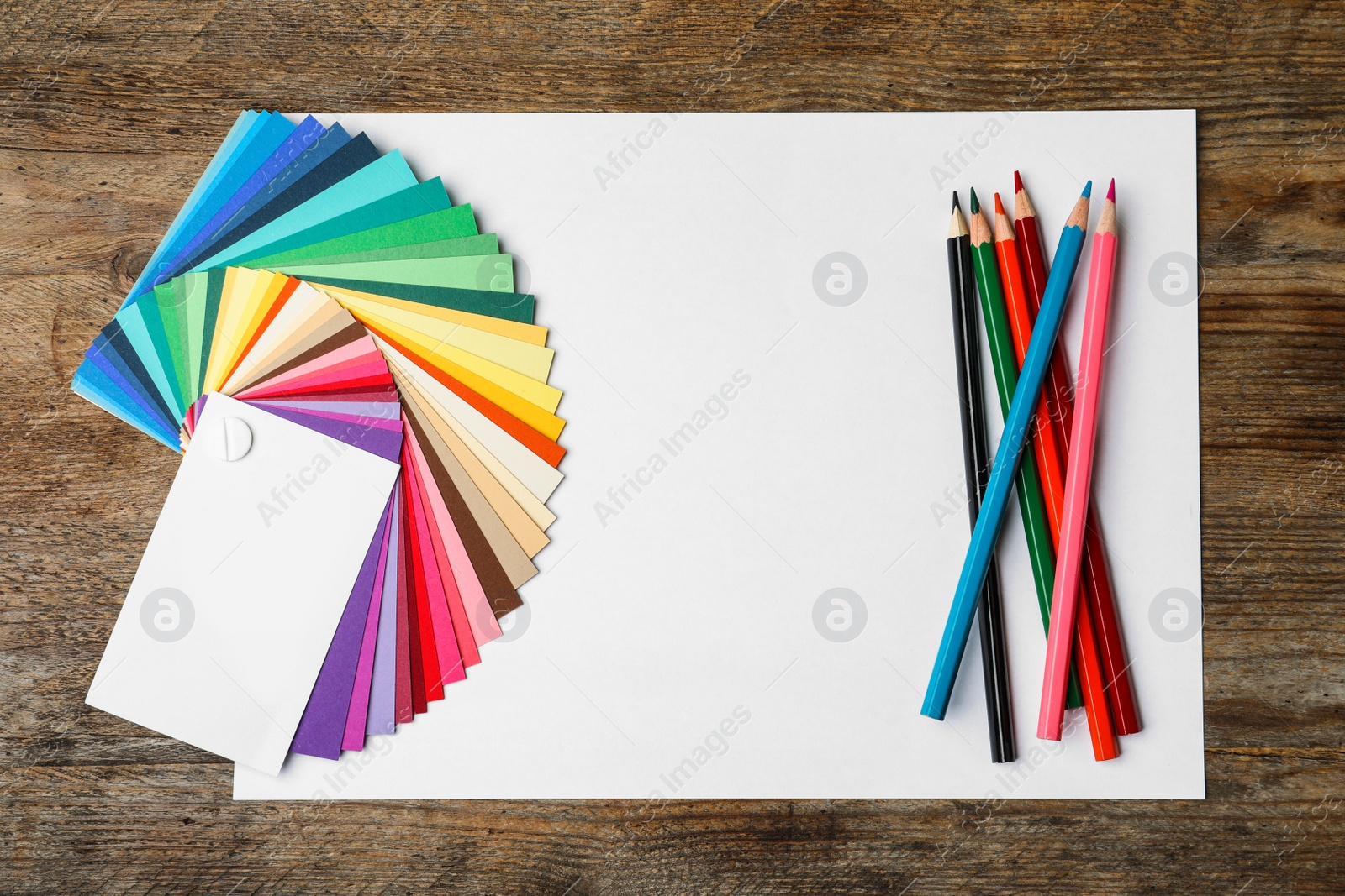 Photo of Color palette, pencils and blank paper sheet on wooden background, flat lay. Space for text