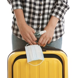 Photo of Woman with suitcase, antiseptic spray and protective mask on white background, closeup. Travelling during coronavirus pandemic