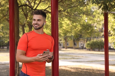 Photo of Young man with wireless headphones and mobile device listening to music on sports ground. Space for text