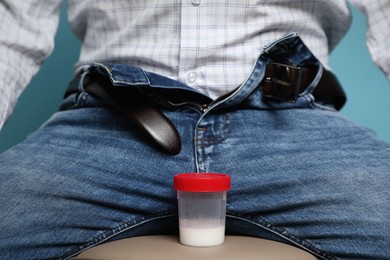 Photo of Donor with unzipped pants and container of sperm sitting on stool, closeup
