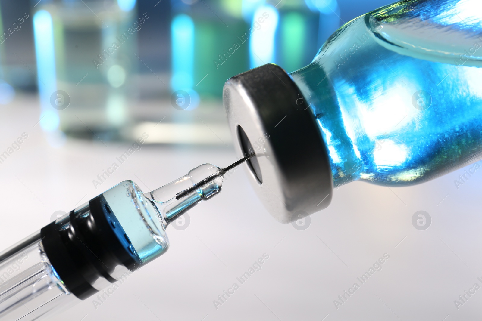 Photo of Filling syringe with vaccine from vial on blurred background, closeup