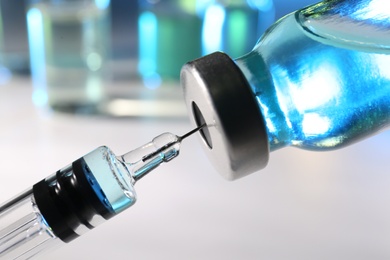 Filling syringe with vaccine from vial on blurred background, closeup