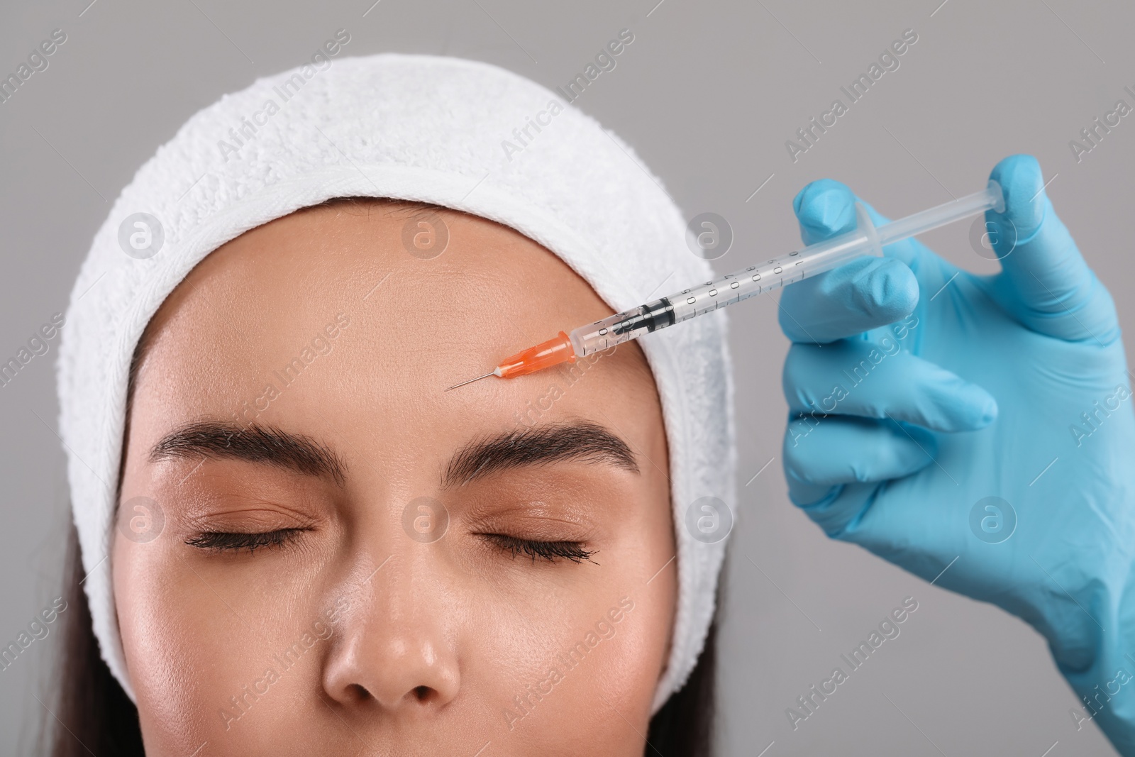 Photo of Doctor giving facial injection to young woman on light grey background, closeup. Cosmetic surgery