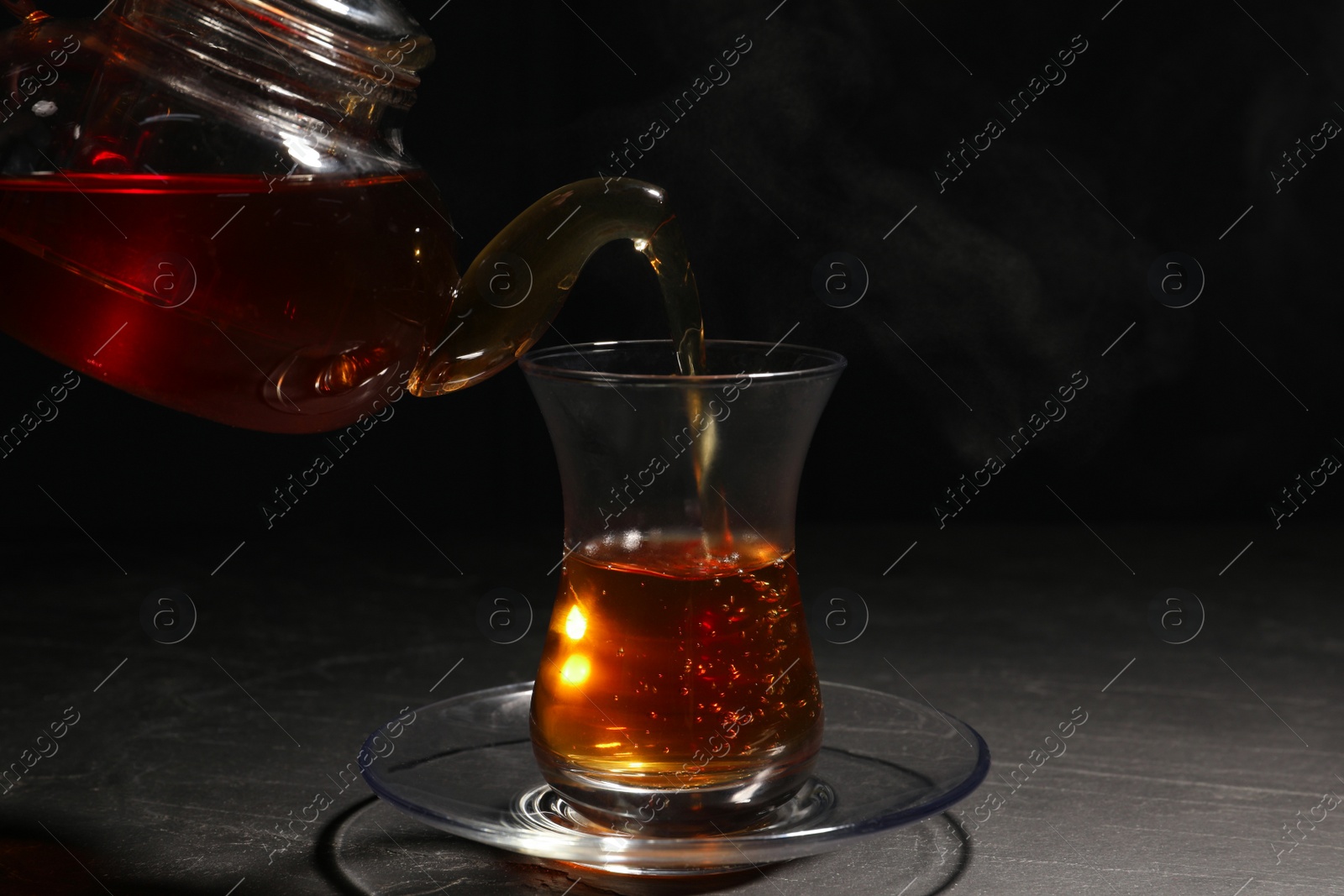 Photo of Pouring traditional Turkish tea from pot into glass on black table