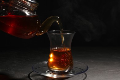 Photo of Pouring traditional Turkish tea from pot into glass on black table