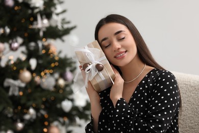 Photo of Happy woman with gift box near Christmas tree indoors