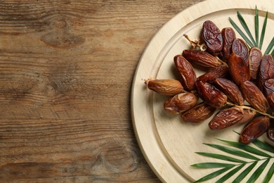 Sweet dried dates with green leaves on wooden table, top view. Space for text