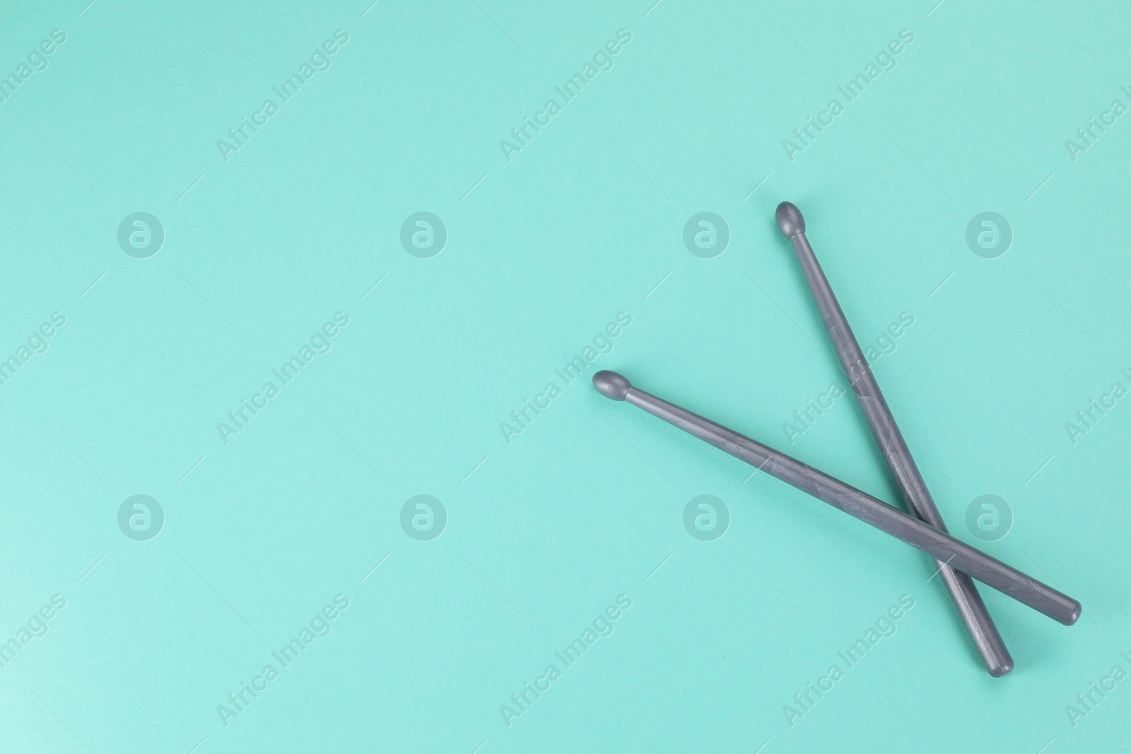 Photo of Two grey drumsticks on turquoise background, top view. Space for text