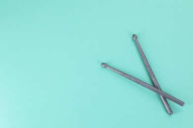 Photo of Two grey drumsticks on turquoise background, top view. Space for text