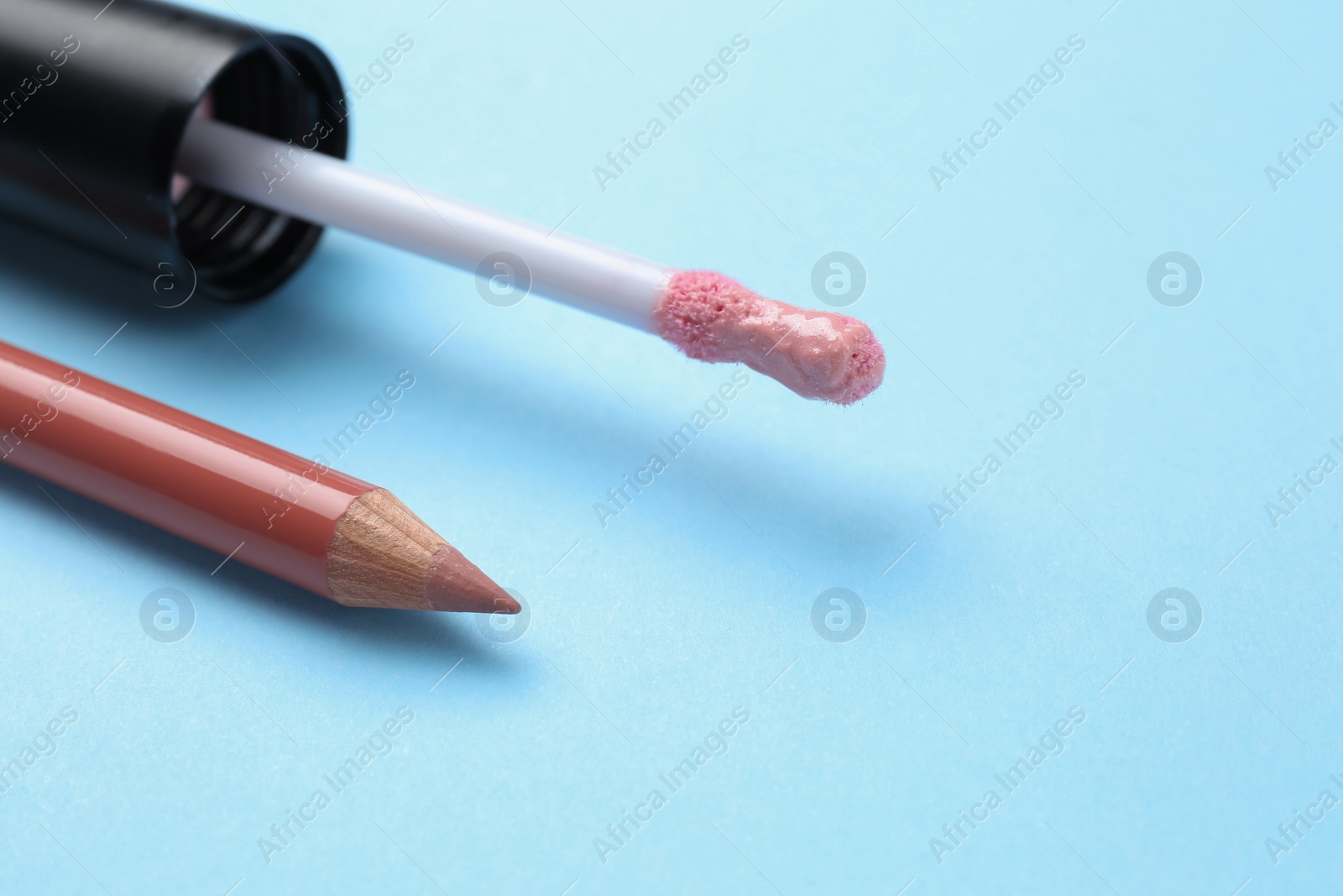 Photo of Lip pencil and brush of liquid lipstick on light blue background, closeup view with space for text. Cosmetic product