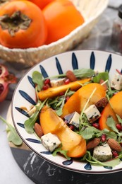 Photo of Tasty salad with persimmon, blue cheese, pomegranate and almonds served on white table, closeup