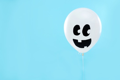 Photo of White balloon with drawing of happy face on blue background, space for text. Halloween party