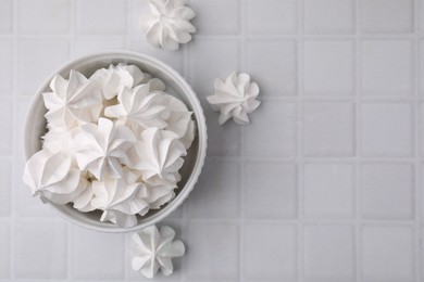 Tasty meringue cookies in bowl on white tiled table. Space for text