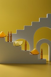Photo of Stylish presentation of skincare ampoules with vitamin C and citrus slices on yellow background