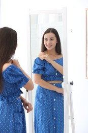 Beautiful young woman looking at herself in large mirror indoors