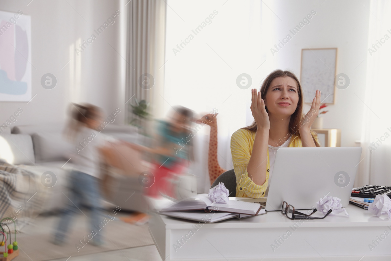 Image of Children disturbing overwhelmed woman in living room. Working from home during quarantine