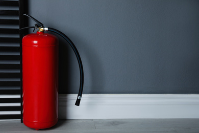 Fire extinguisher near grey wall indoors. Space for text