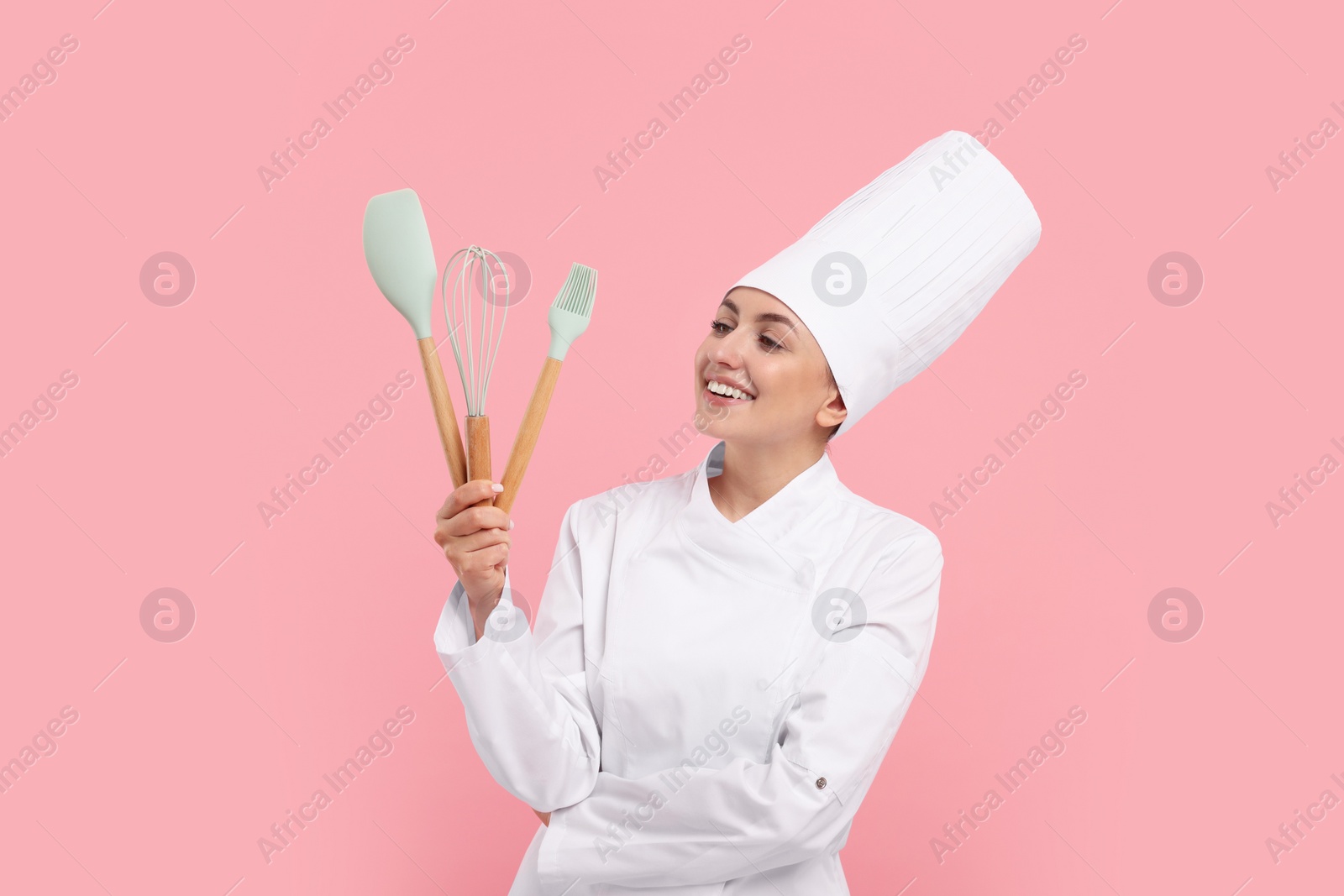 Photo of Happy confectioner in uniform holding professional tools on pink background