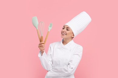 Happy confectioner in uniform holding professional tools on pink background