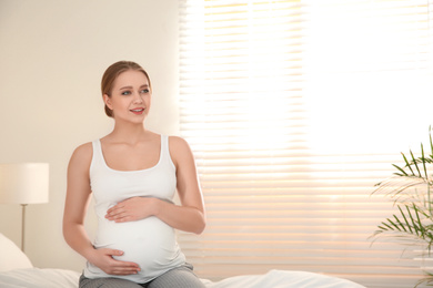 Young pregnant woman on bed at home. Space for text