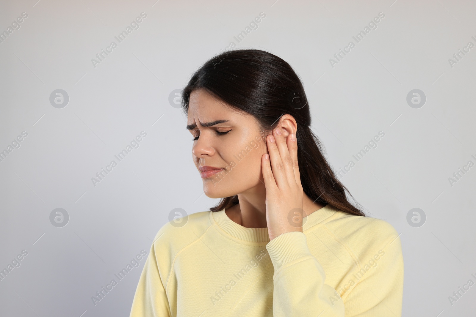 Photo of Young woman suffering from ear pain on light grey background