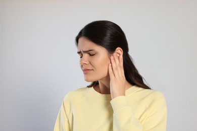 Young woman suffering from ear pain on light grey background