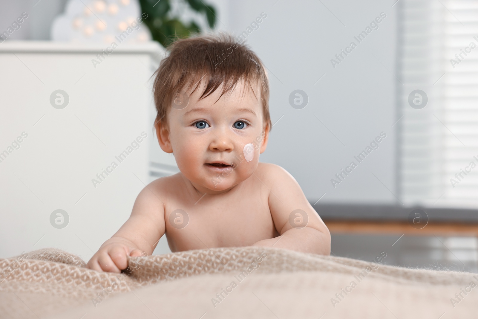 Photo of Cute little baby with moisturizing cream on face indoors