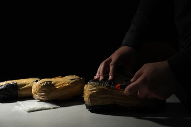 Photo of Smuggling and drug trafficking. Man opening package of narcotics with box cutter at light table against black background, closeup. Space for text