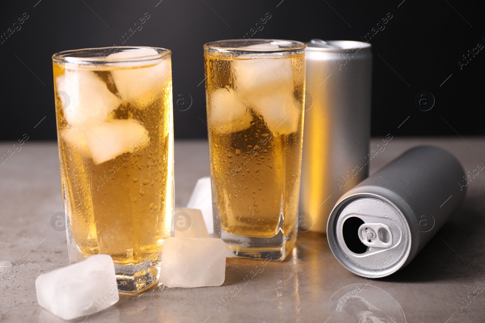 Photo of Tasty energy drink with ice cubes in glasses and aluminium cans on grey table, closeup