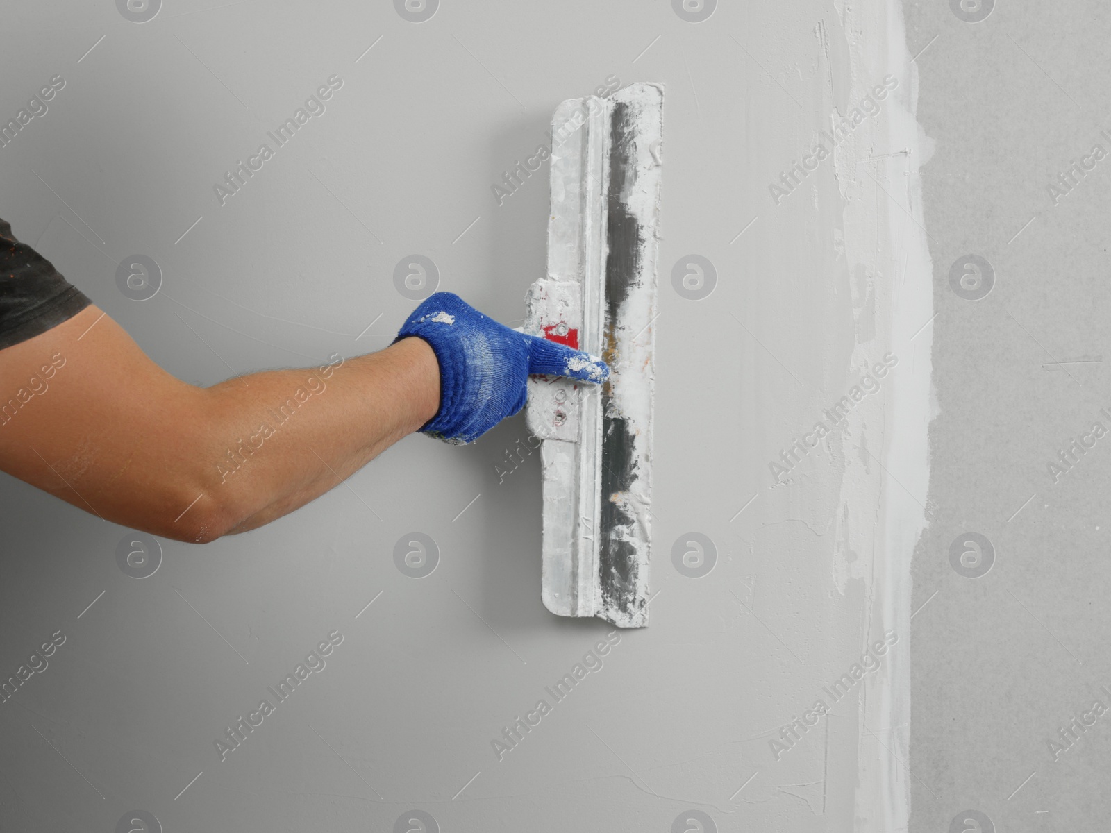 Photo of Professional worker plastering wall with putty knife, closeup