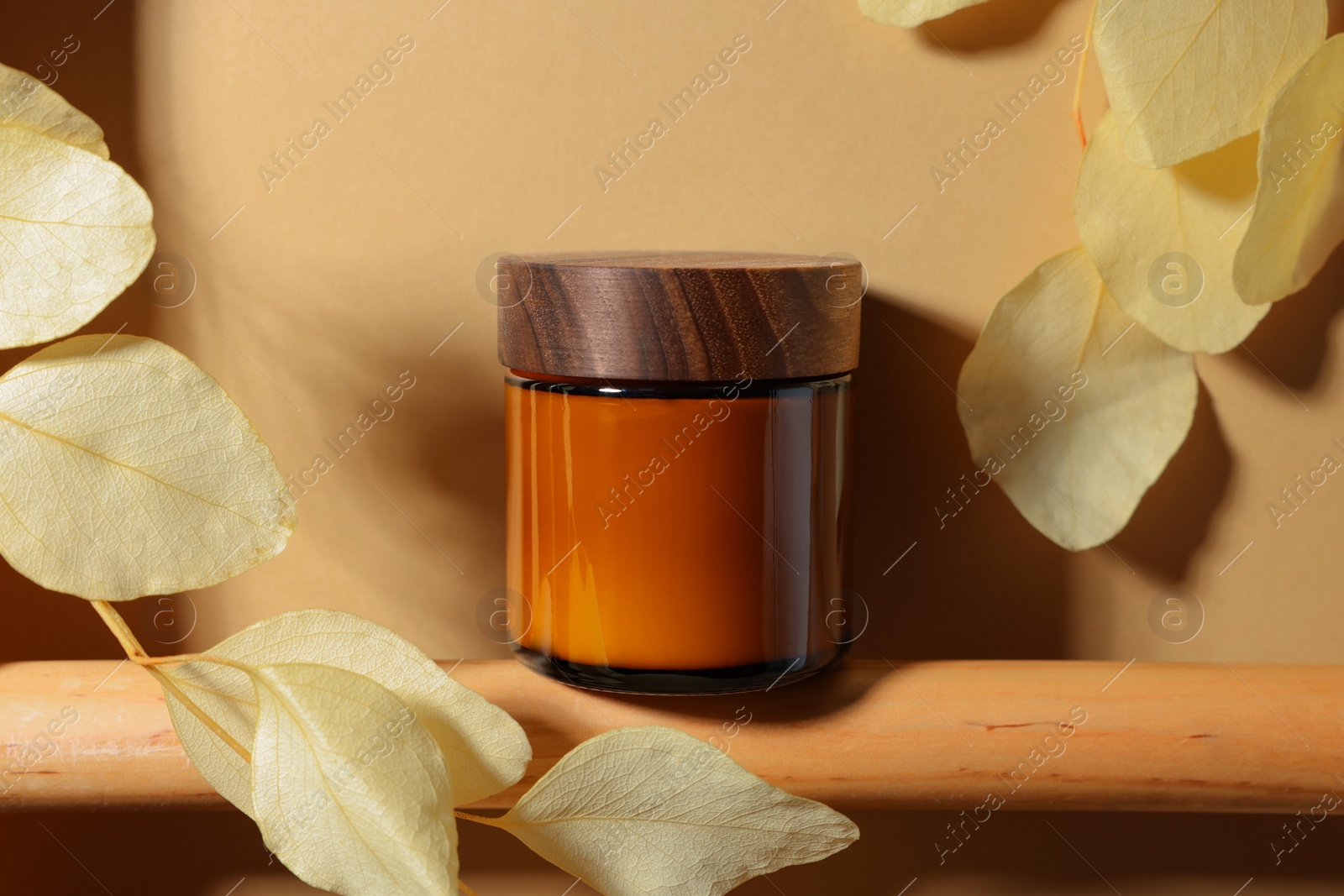 Photo of Jar of luxury cream and dried leaves on dark beige background