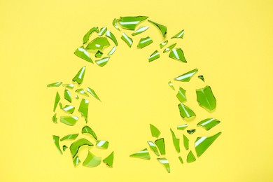 Recycling symbol made of glass pieces on yellow background, flat lay
