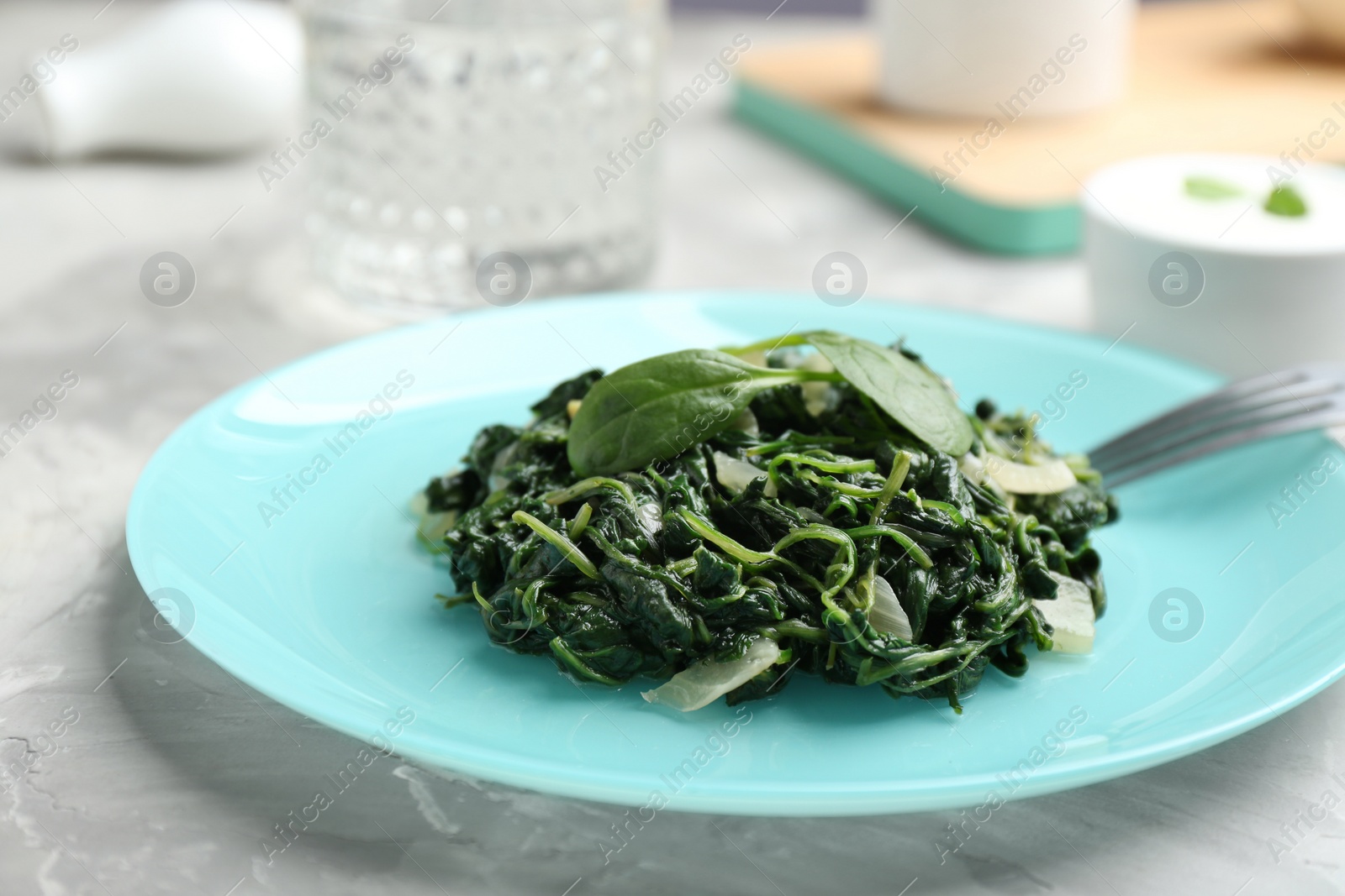 Photo of Plate with cooked spinach and fork on grey table, closeup. Healthy food