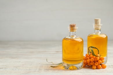 Natural sea buckthorn oil and fresh berries on white wooden table. Space for text