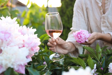 Photo of Woman with glass of rose wine in peony garden, closeup
