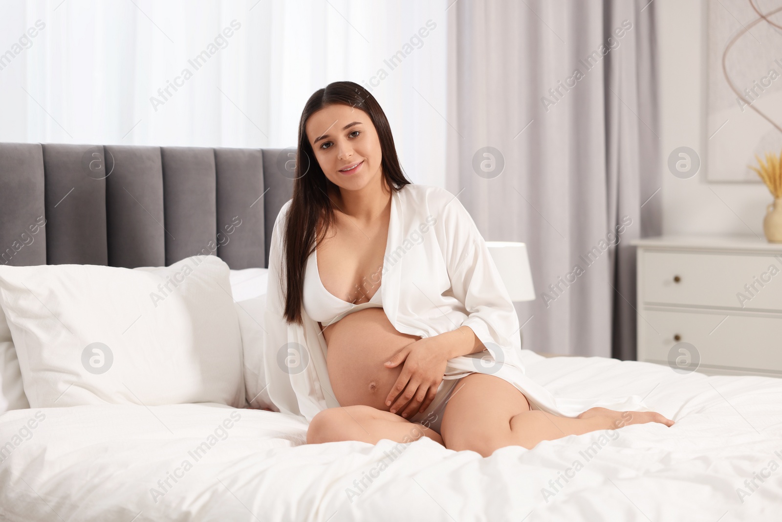 Photo of Beautiful pregnant woman in stylish comfortable underwear and robe on bed at home