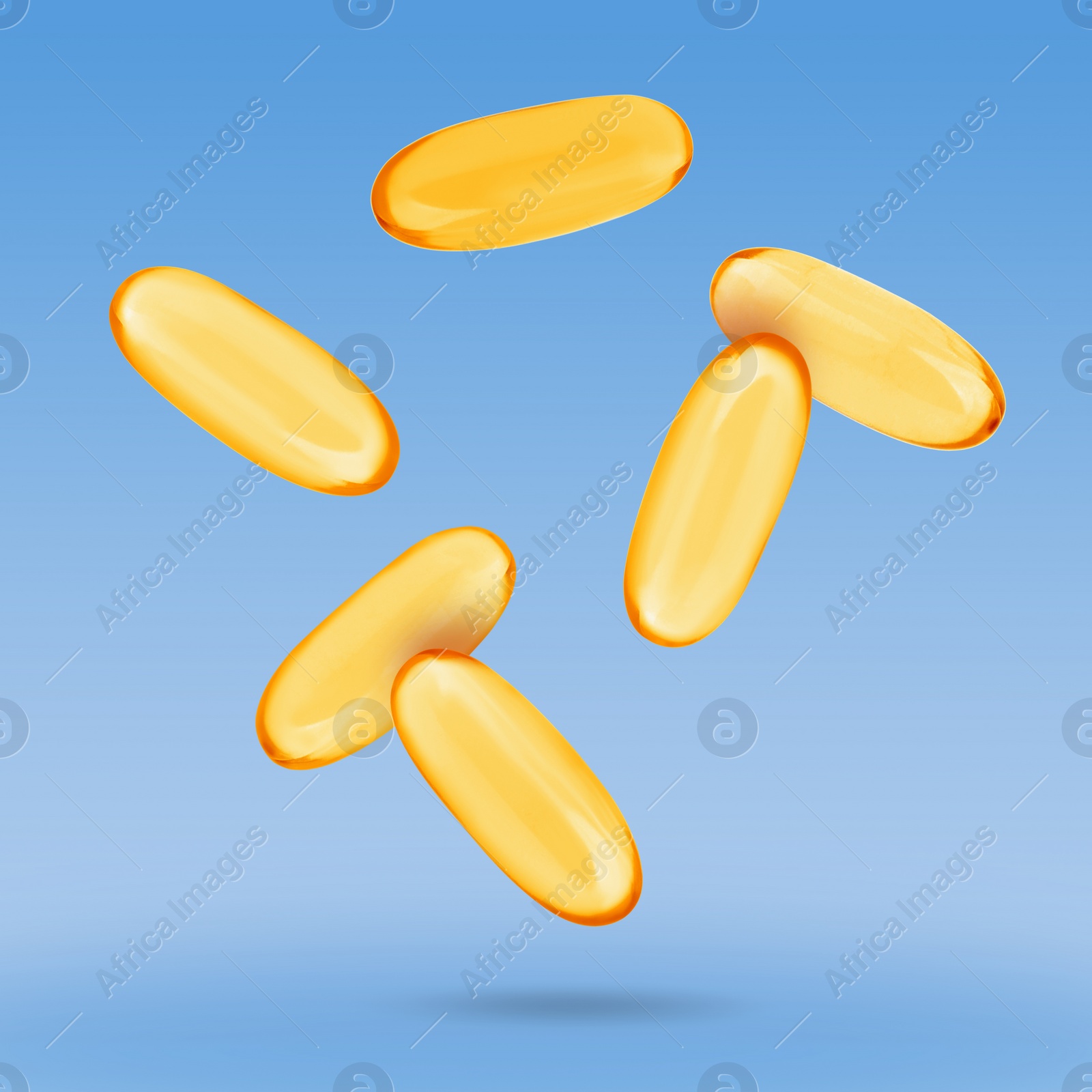 Image of Vitamin. Softgel capsules falling on blue gradient background